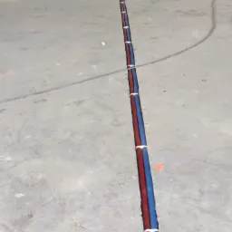 Instalacja ogrzewania podłogowego w trakcie realizacji: rury grzewcze czerwone i niebieskie ułożone w wyżłobieniu w betonie, zabezpieczone białymi opaskami, widoczne ślady po wierceniu w ścianie...