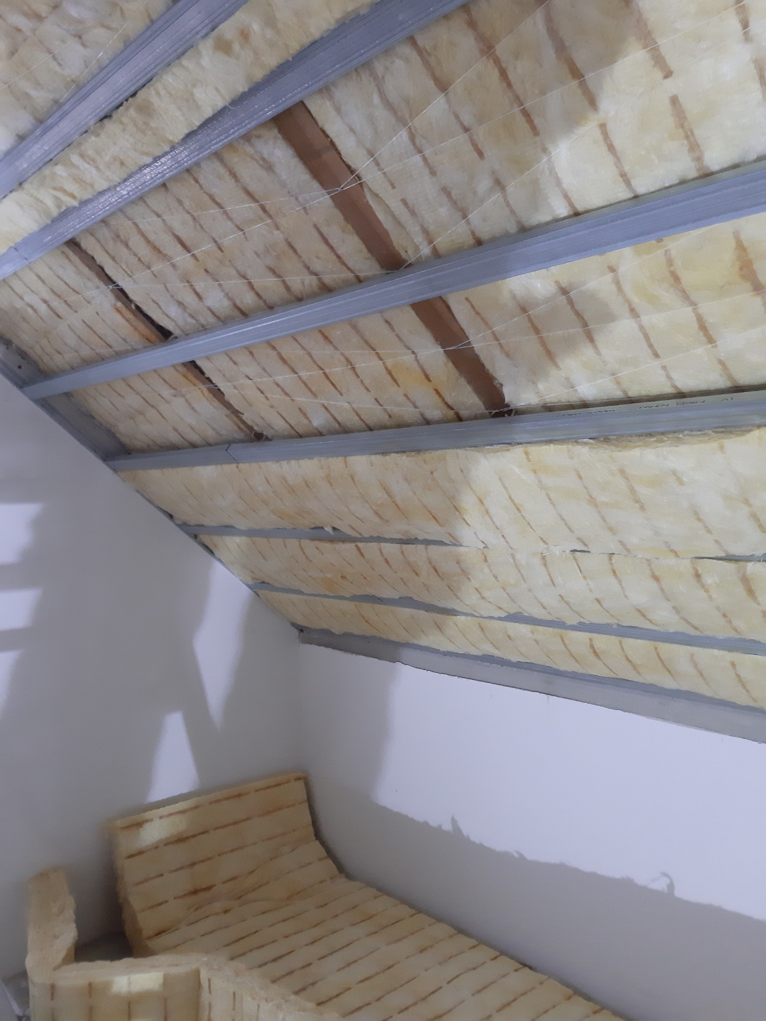 Poddasze w trakcie ocieplania wełną mineralną, widoczne metalowe profile konstrukcyjne i fragment ściany.