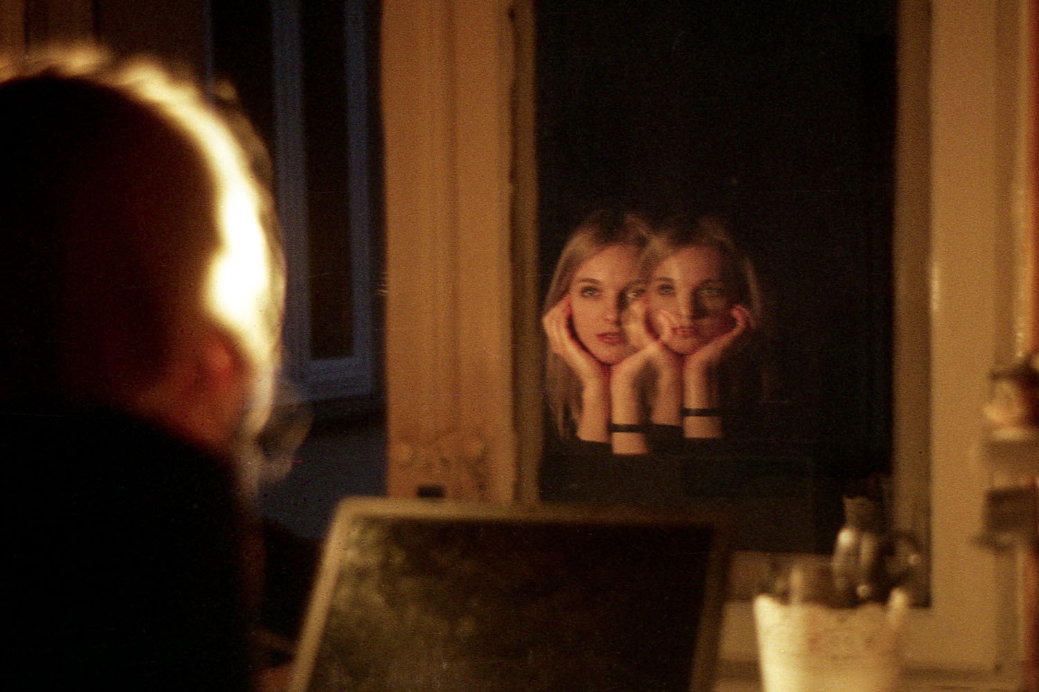 Portret kobiety w lustrze z efektem podwójnego odbicia, ciepłe oświetlenie, widoczne odbicie twarzy w dłoniach.