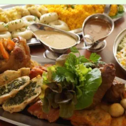 Uroczysty półmisek z golonką, kluskami śląskimi, pierogami ze szpinakiem, sosem w sosjerkach i surówką z kapusty na drewnianym stole.