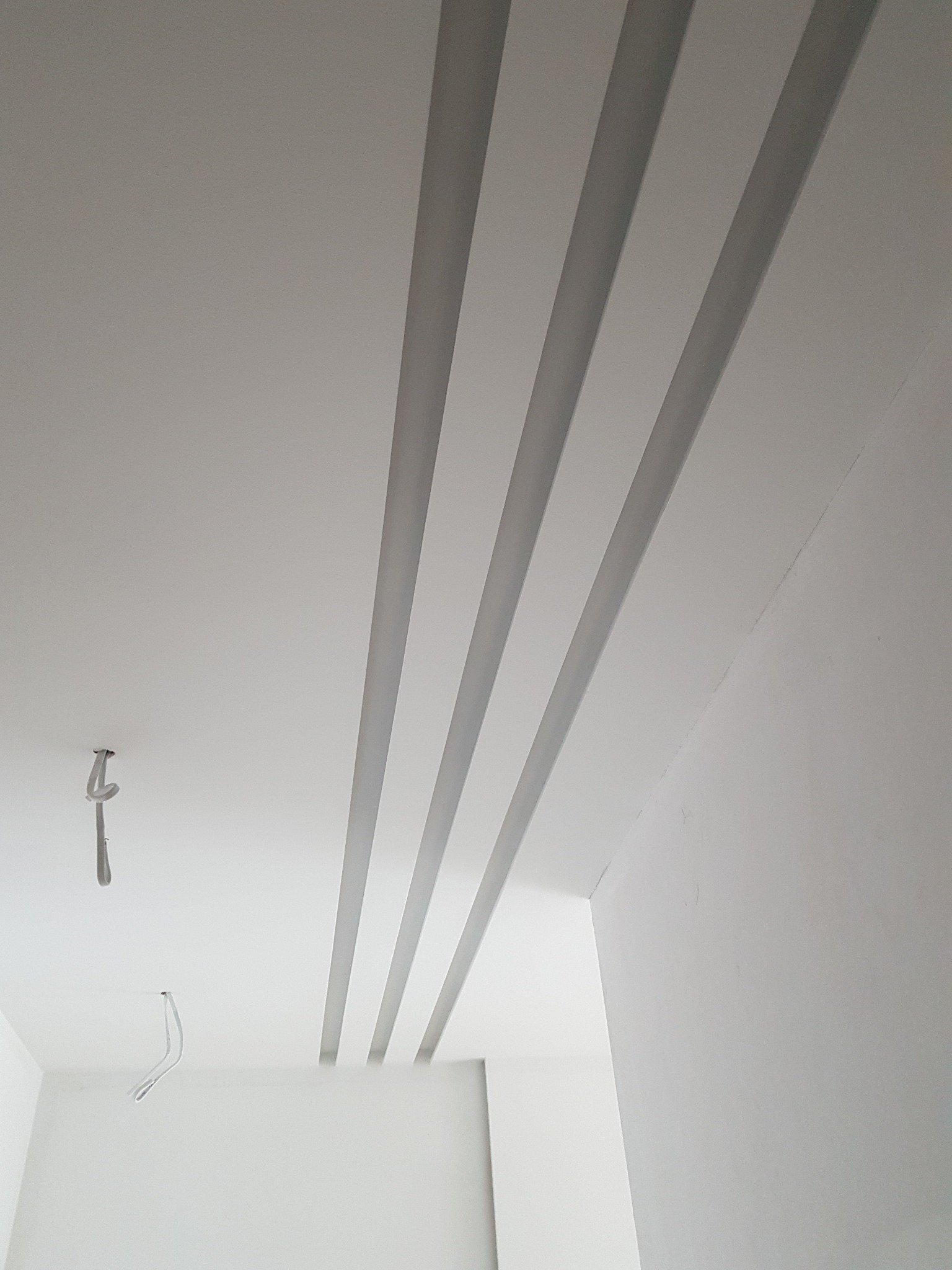 Biały sufit z czterema równoległymi, wpuszczonymi pasami oświetleniowymi, widoczne kable wystające z sufitu w rogu pomieszczenia.