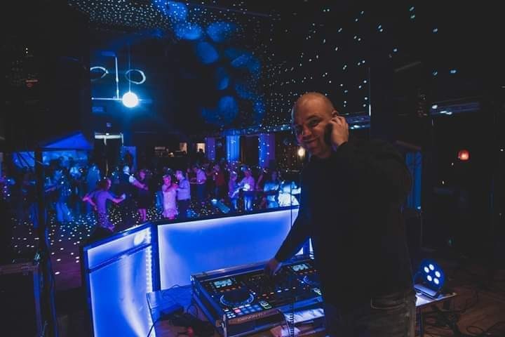 DJ rozmawia przez telefon podczas występu, w tle tańczący tłum i dekoracyjne oświetlenie w odcieniach niebieskiego.