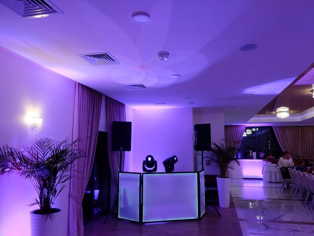 Sala bankietowa oświetlona fioletowymi światłami, z nagłośnieniem i oświetleniem DJ-skim, roślinami w donicach i widocznymi krzesłami dla gości.