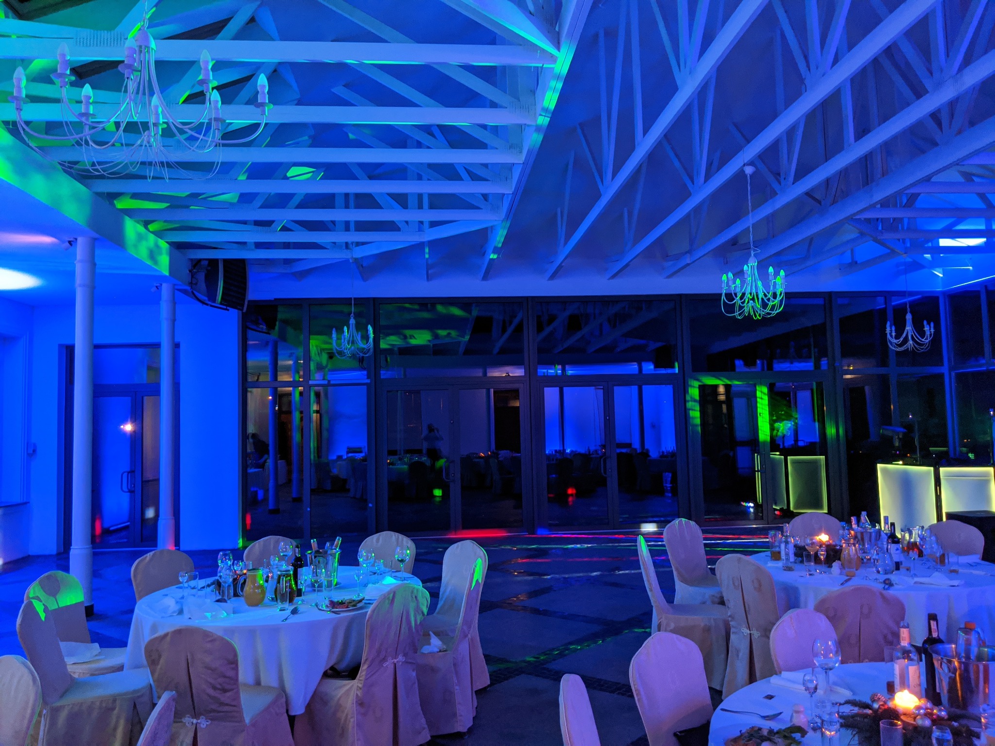 Uroczysta sala bankietowa w Warszawie, oświetlona niebieskim i zielonym światłem, z okrągłymi stołami nakrytymi białymi obrusami i eleganckimi krzesłami, przygotowana na przyjęcie.