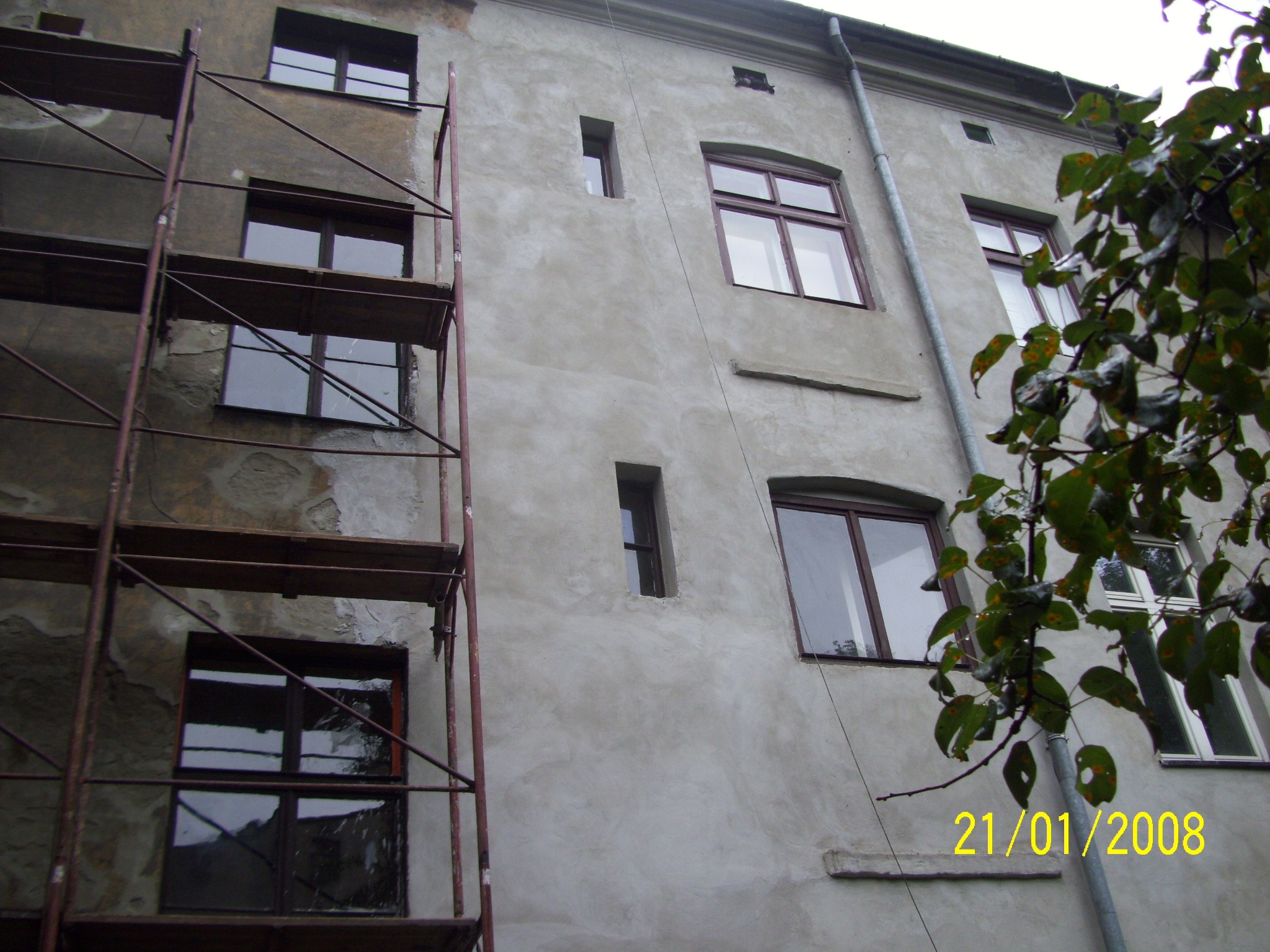 Stare, szare budynek w trakcie tynkowania, z widocznym rusztowaniem i fragmentem rynny, ujęcie z dołu.