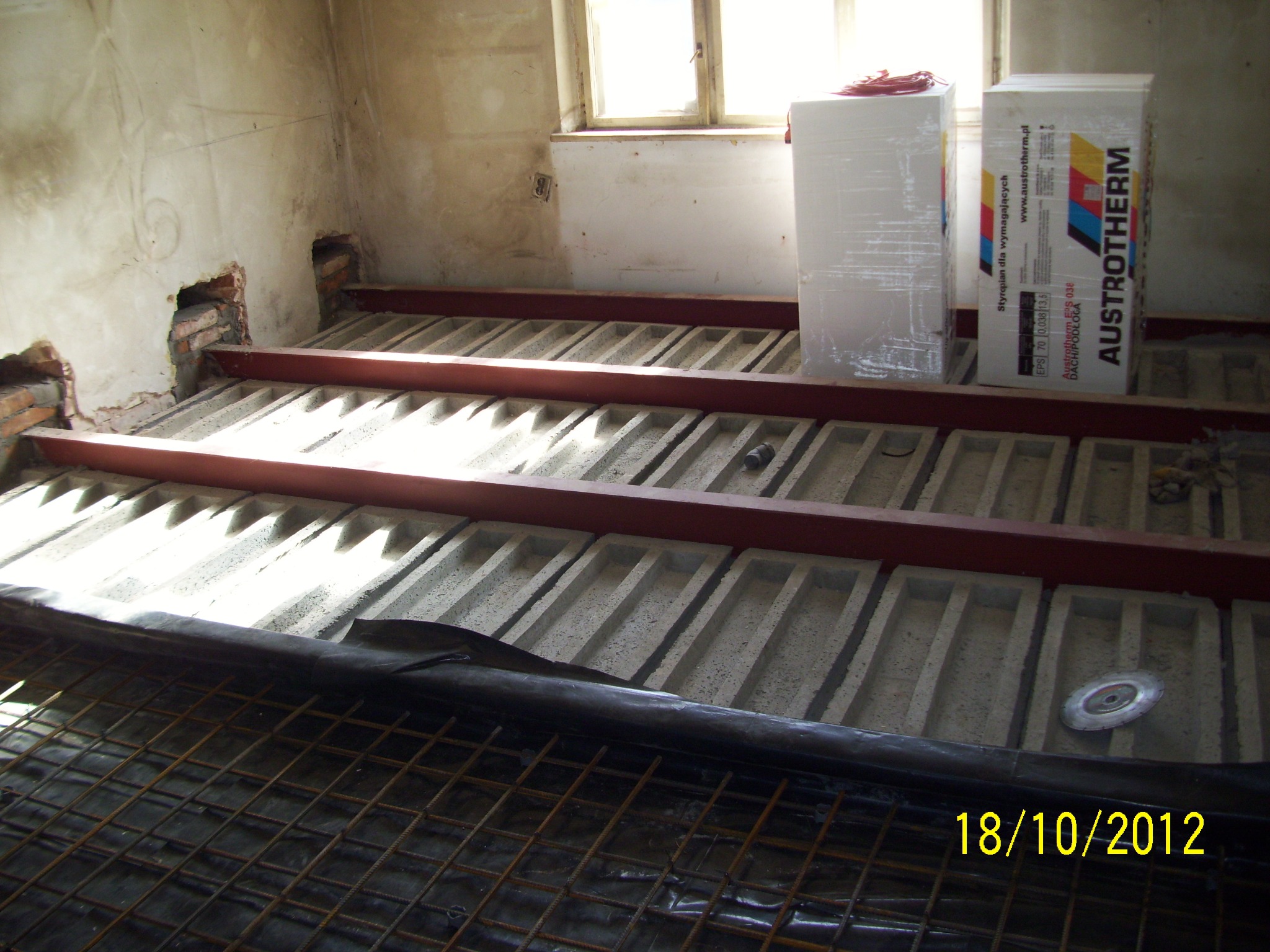 Przygotowanie do ocieplenia poddasza: stalowe belki, betonowe pustaki, folia paroizolacyjna, siatka zbrojeniowa i paczki styropianu Austrotherm w surowym wnętrzu.