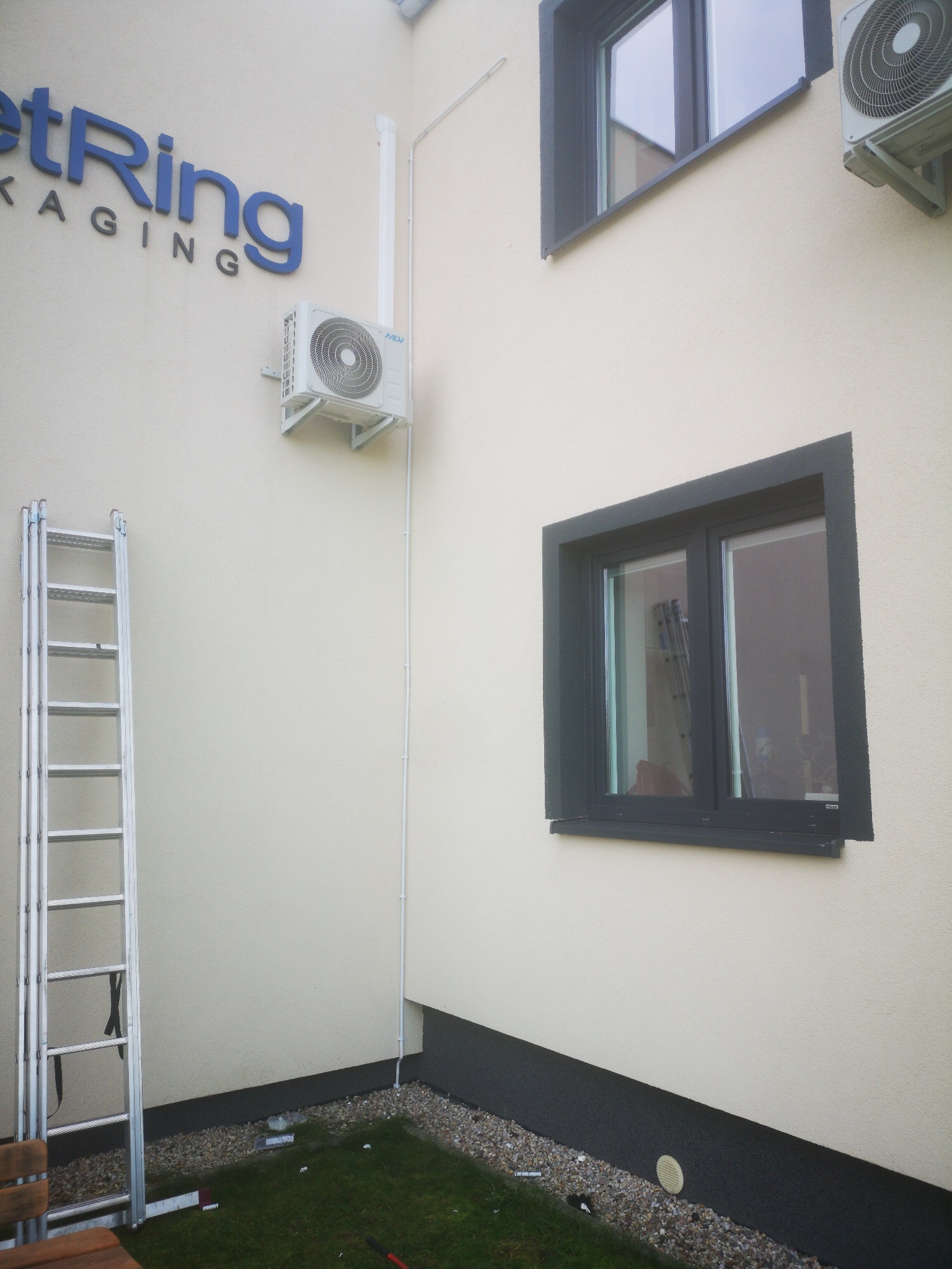 Zewnętrzny montaż klimatyzacji MDV na elewacji budynku firmy z widoczną drabiną aluminiową i oknami z ciemnymi ramami.