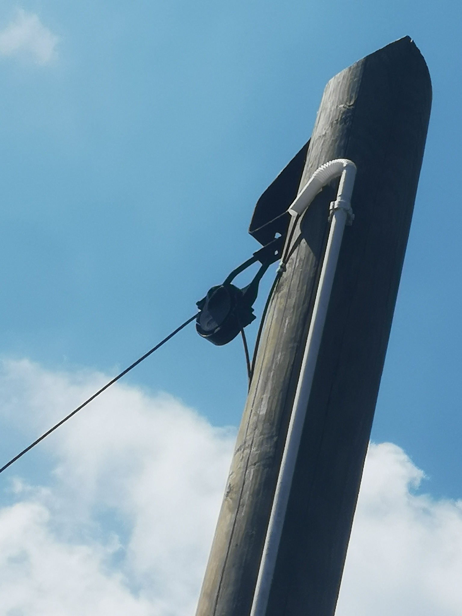 Słup telekomunikacyjny z zamontowanym osprzętem, widok z dołu na tle błękitnego nieba z chmurami.