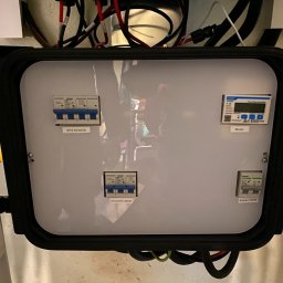 Sun-Spot Elektro Montaż - Rozdzielnica elektryczna z zabezpieczeniami i licznikiem energii, widoczne bezpieczniki EPS RCMCB, Grid(INV) MCB, Battery MCB oraz licznik CHNT, okablowanie w górnej części obudowy.