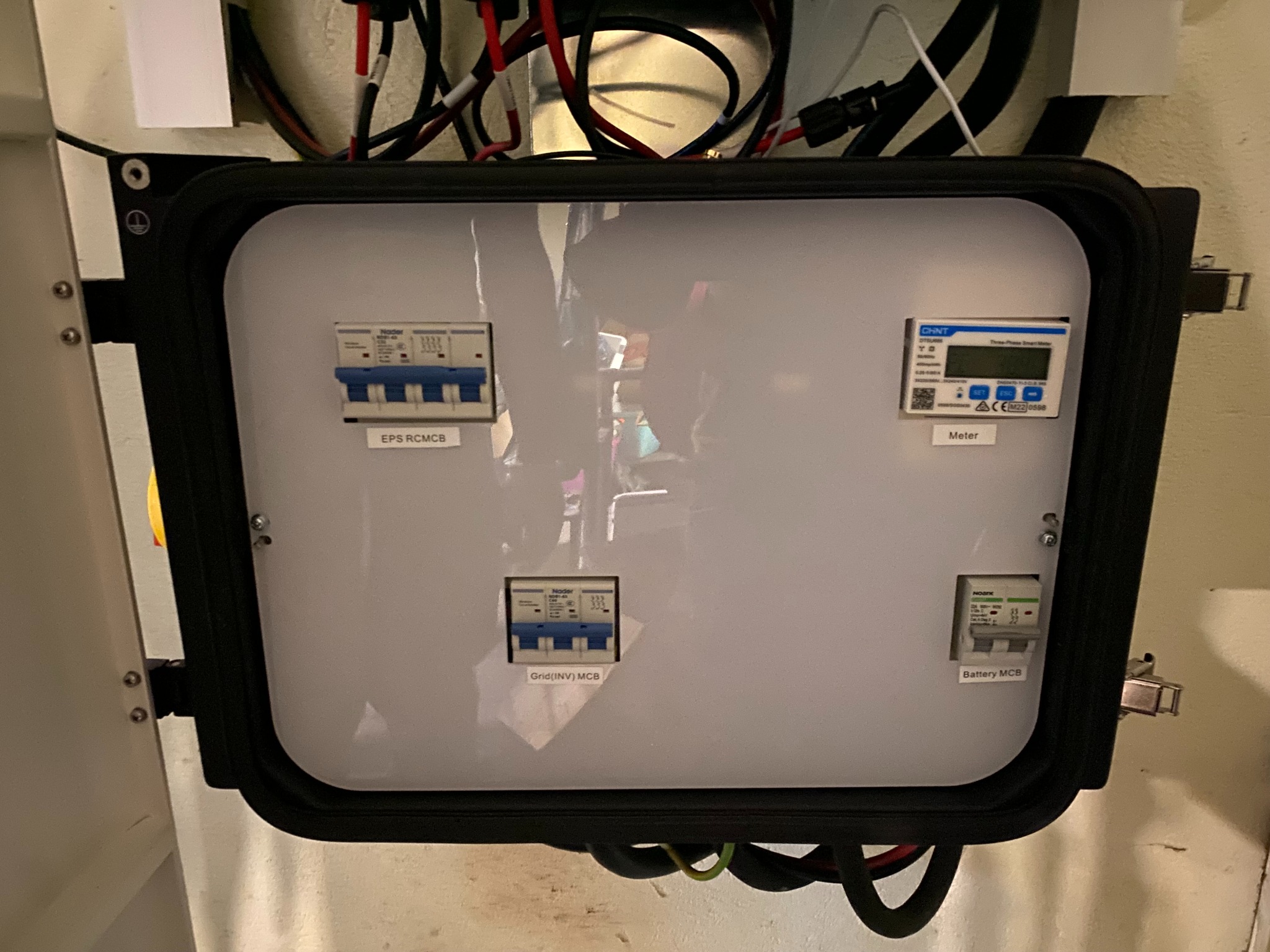 Rozdzielnica elektryczna z zabezpieczeniami i licznikiem energii, widoczne bezpieczniki EPS RCMCB, Grid(INV) MCB, Battery MCB oraz licznik CHNT, okablowanie w górnej części obudowy.