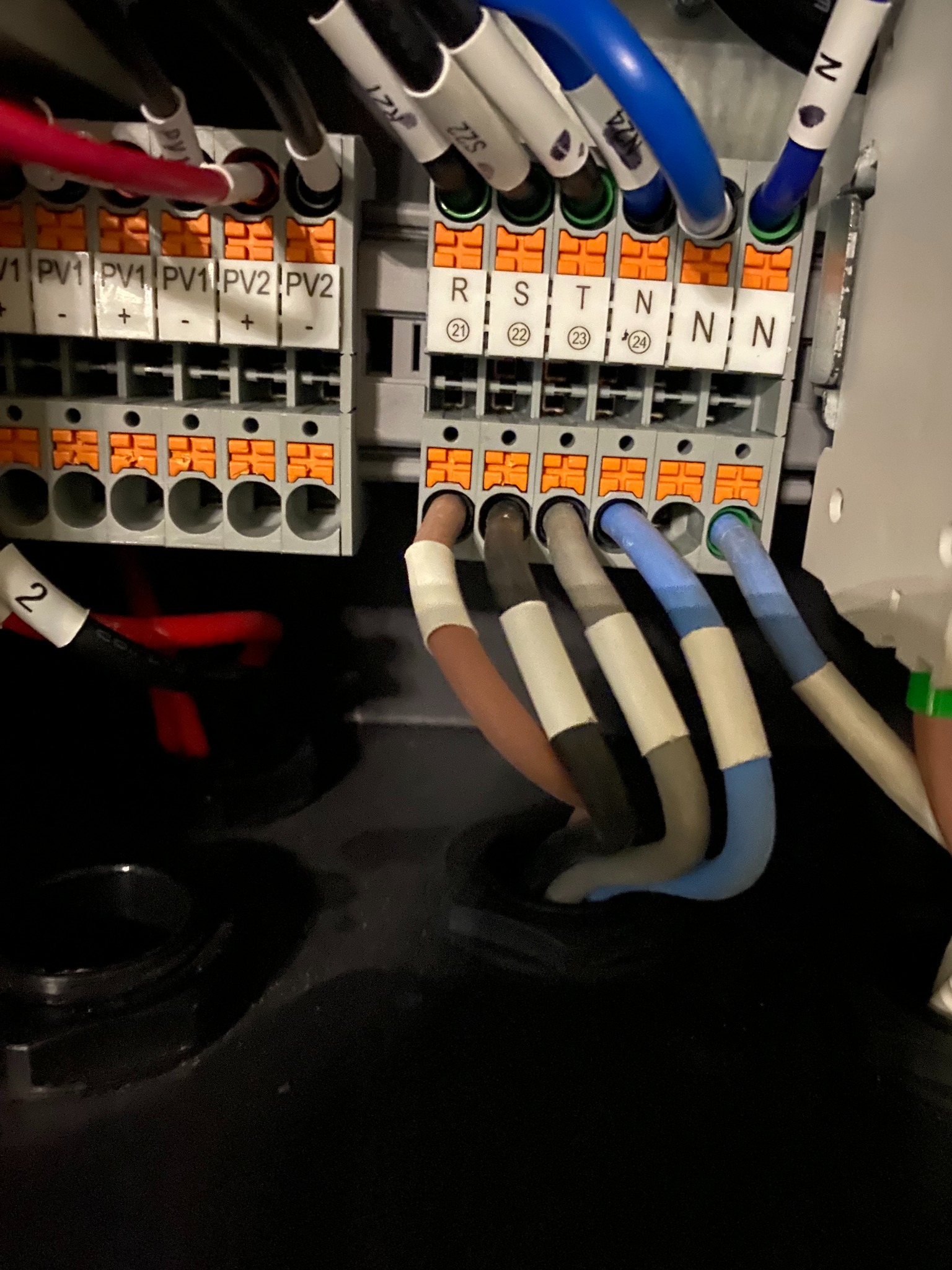 Szczegółowe ujęcie przewodów elektrycznych podłączonych do listwy zaciskowej w rozdzielnicy, z widocznymi oznaczeniami PV1, PV2 oraz R, S, T, N.
