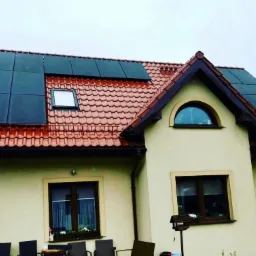 Dom jednorodzinny z panelami słonecznymi na czerwonym dachu, widok z przodu, pochmurne niebo w tle.