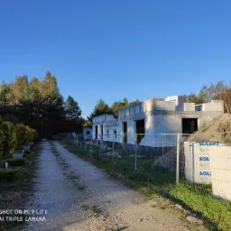 Stan surowy otwarty domu z białych bloczków, widok z drogi dojazdowej, materiały budowlane Solbet za ogrodzeniem.