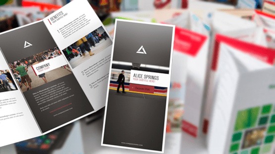 Stos ulotek i broszur z grafikami i tekstem, na białym tle, widoczne z góry pod kątem.