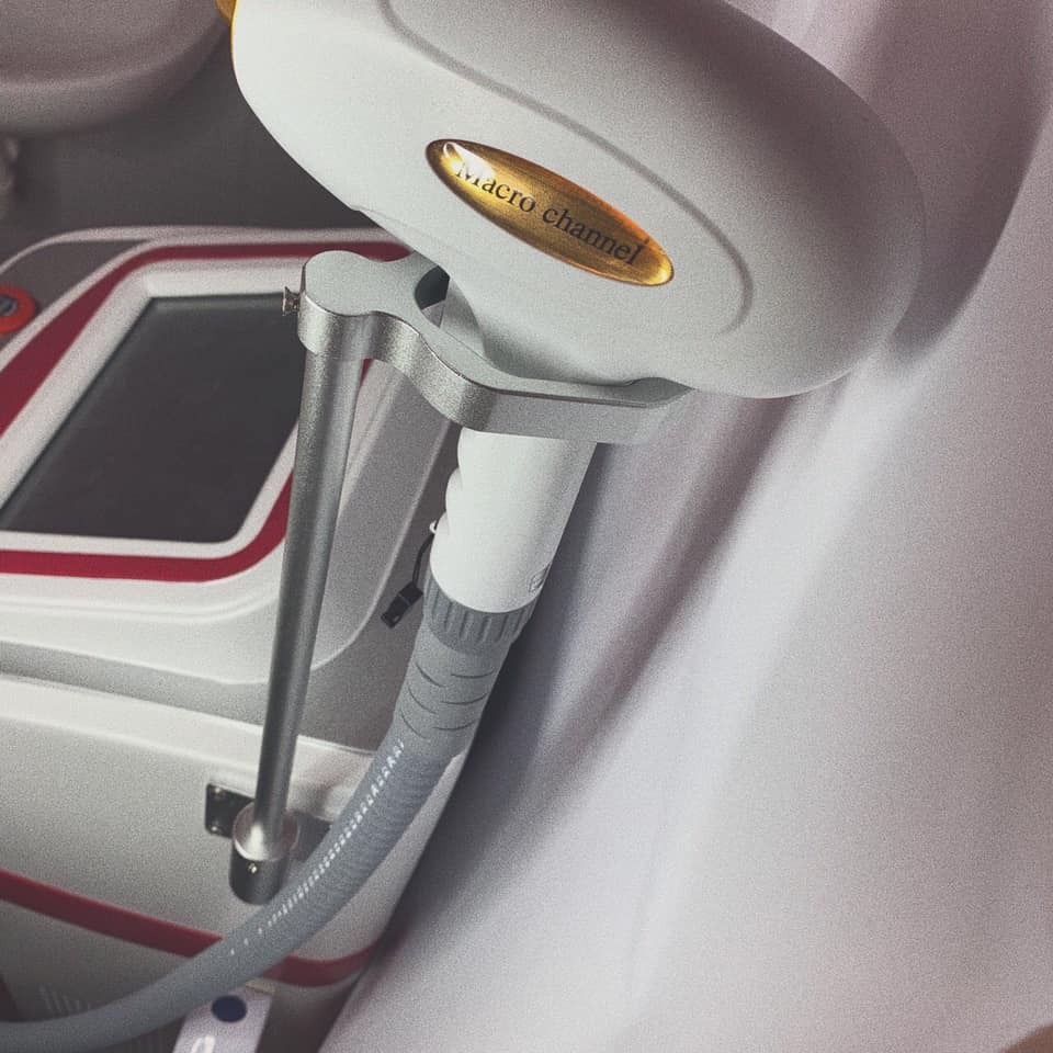 Urządzenie do zabiegów kosmetycznych z głowicą 'macro channel' i szarą rurką, ustawione na białym tle. Widoczny fragment panelu sterowania z czerwonymi akcentami.
