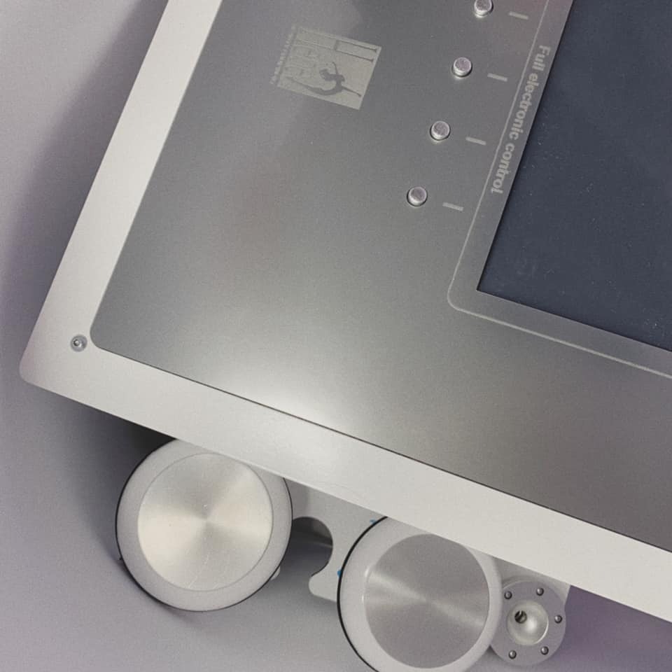 Panel sterowania urządzenia kosmetycznego z wyświetlaczem, srebrną obudową i pokrętłami, widoczne logo firmy.