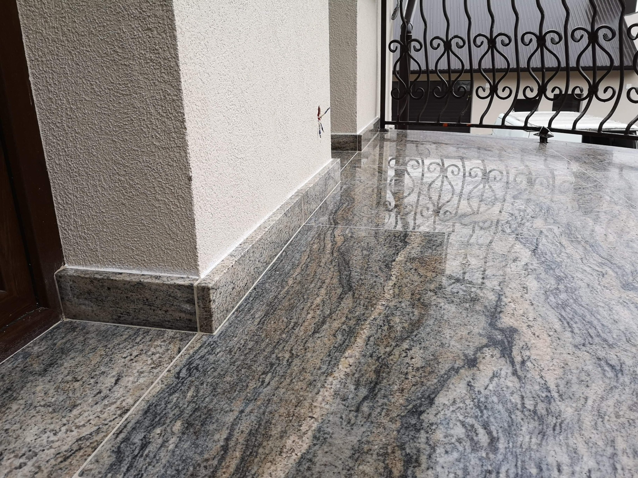 Kamienna podłoga na balkonie z widocznymi detalami wzoru kamienia i listwami przypodłogowymi, odbijająca się metalowa balustrada.