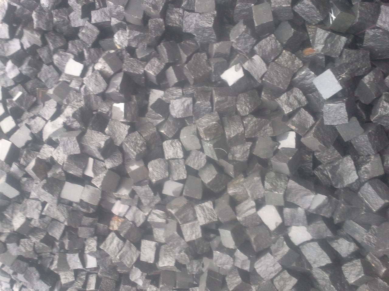 Stos szarych, surowych kostek granitowych o nieregularnych kształtach, widoczny z góry, z lekkim efektem zamglenia.
