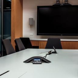 Pro VC Services - Nowoczesna sala konferencyjna z dużym ekranem NEC, głośnikami naściennymi, stołem konferencyjnym z mikrofonami i szarymi krzesłami.