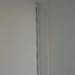 Fragment ściany po szpachlowaniu i malowaniu na biało, widoczny narożnik okna i fragment parapetu.