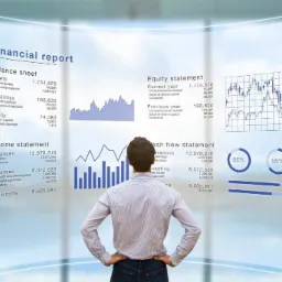 Mężczyzna z tyłu, w koszuli w paski, patrzy na interaktywny ekran z raportem finansowym, wykresami i danymi bilansowymi w nowoczesnym biurze.