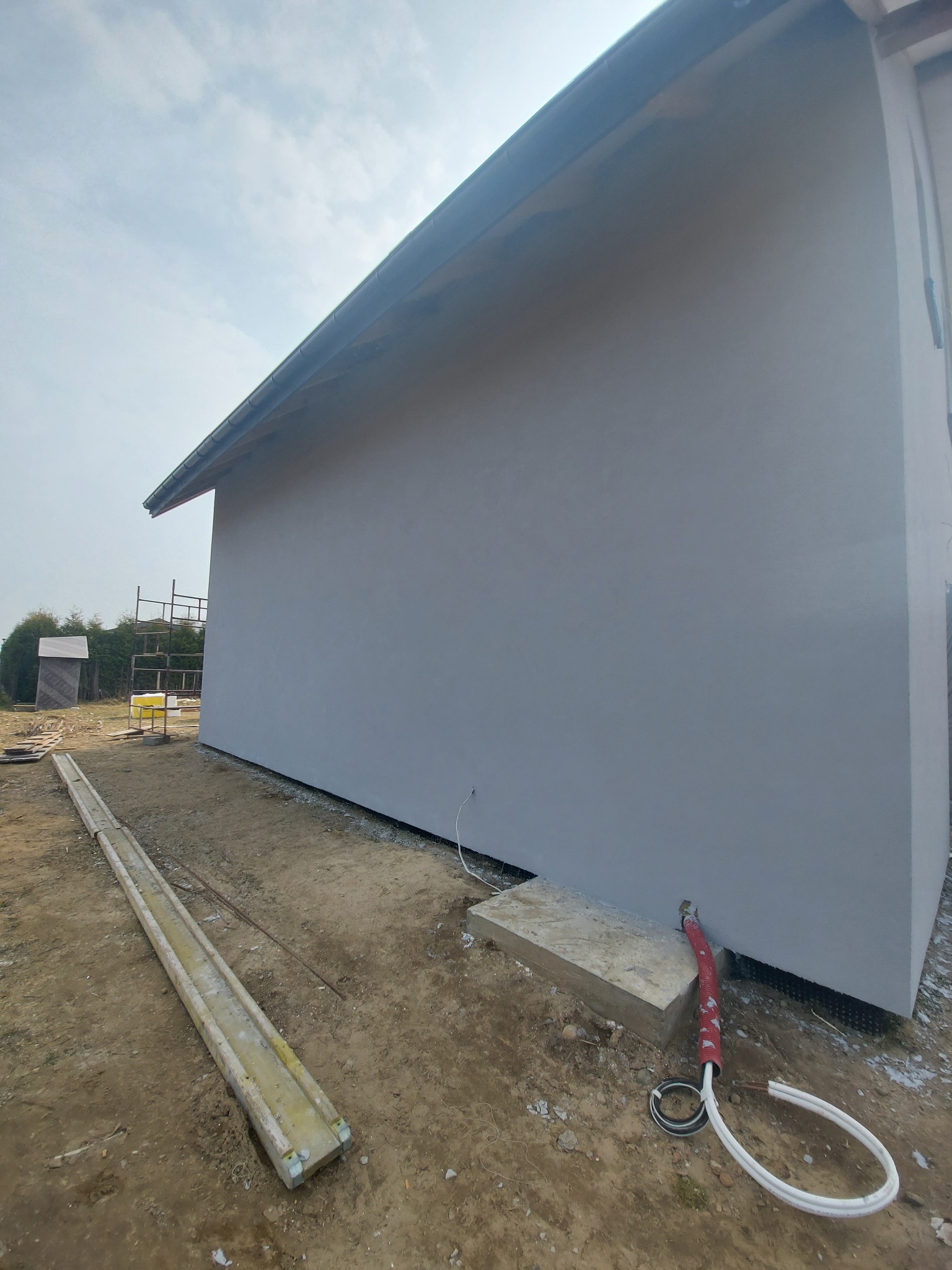 Szara elewacja budynku w Ozorkowie, widoczne kable wystające ze ściany, teren budowy w trakcie prac wykończeniowych.