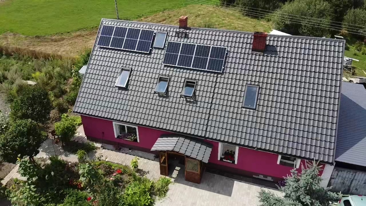 Dom jednorodzinny z szarą dachówką, oknami dachowymi i panelami słonecznymi, widok z lotu ptaka.