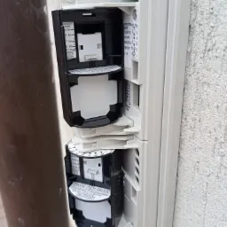 Dwa czujniki ruchu w obudowie, zamontowane na szarej, chropowatej ścianie, z widocznymi ustawieniami zasięgu i kierunku detekcji oraz przewodami elektrycznymi.