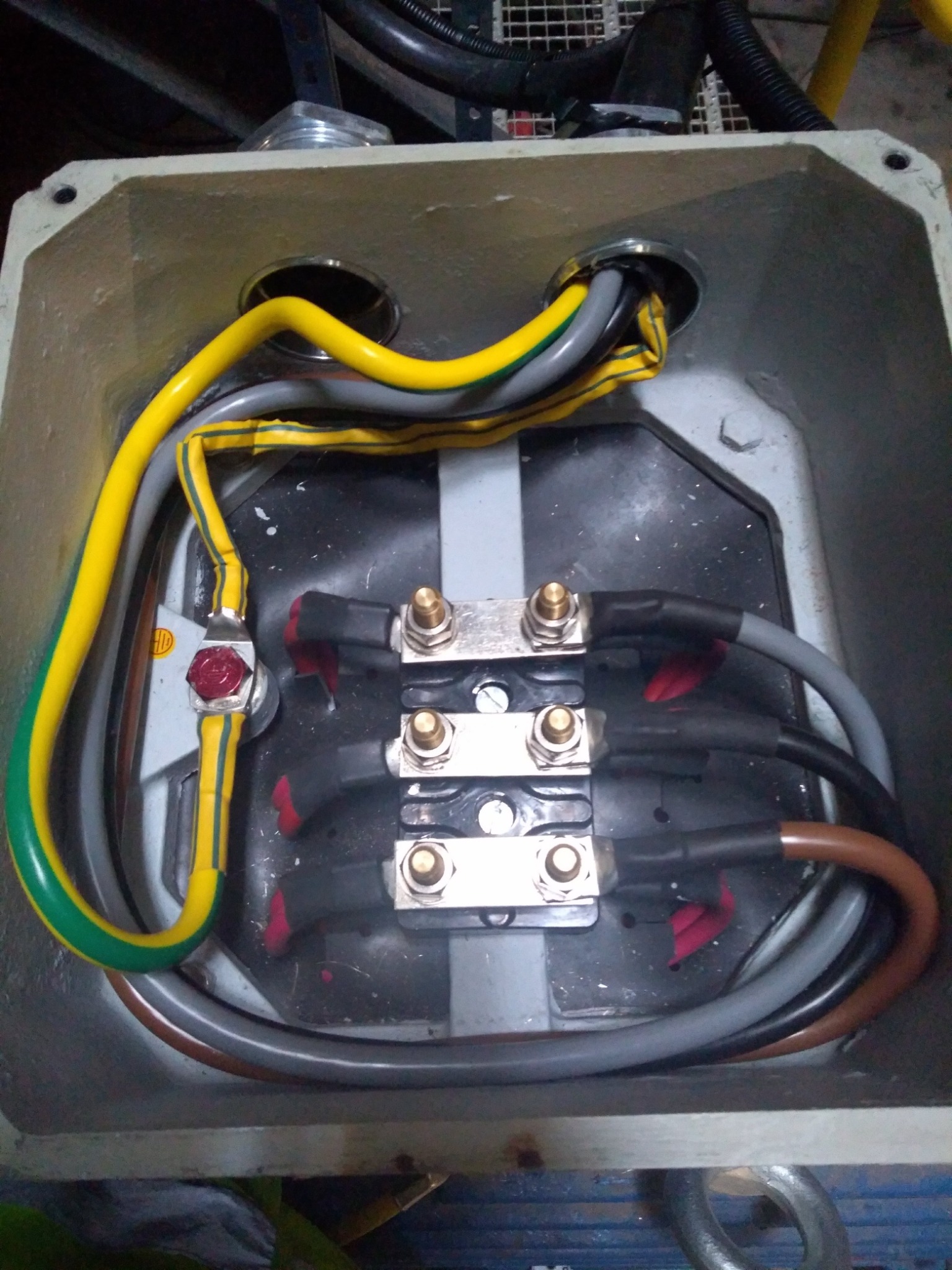 Wnętrze skrzynki elektrycznej z podłączonymi kablami o różnych kolorach, widoczne złącza śrubowe i przewody w izolacji, ułożone wewnątrz metalowej obudowy.