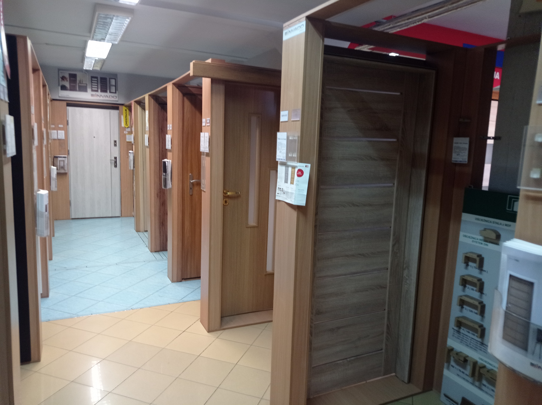 Ekspozycja różnych modeli drzwi wewnętrznych w salonie w Nowym Sączu, widoczne różne kolory i wzory, na podłodze płytki w dwóch odcieniach.