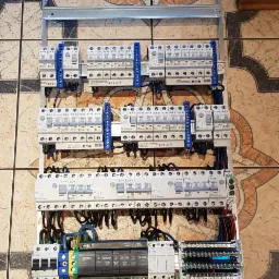 Rozdzielnica elektryczna z zabezpieczeniami przepięciowymi Eaton, zamontowana na szynie, widoczna na tle płytek podłogowych z wzorem kwiatowym.