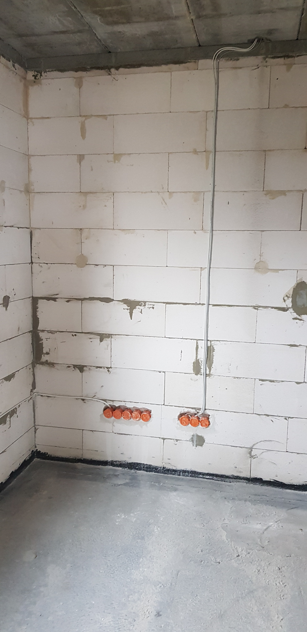 Wewnętrzne ściany z betonu komórkowego w surowym stanie z widocznymi puszkami instalacyjnymi i przewodami elektrycznymi wystającymi ze ściany pod sufitem.