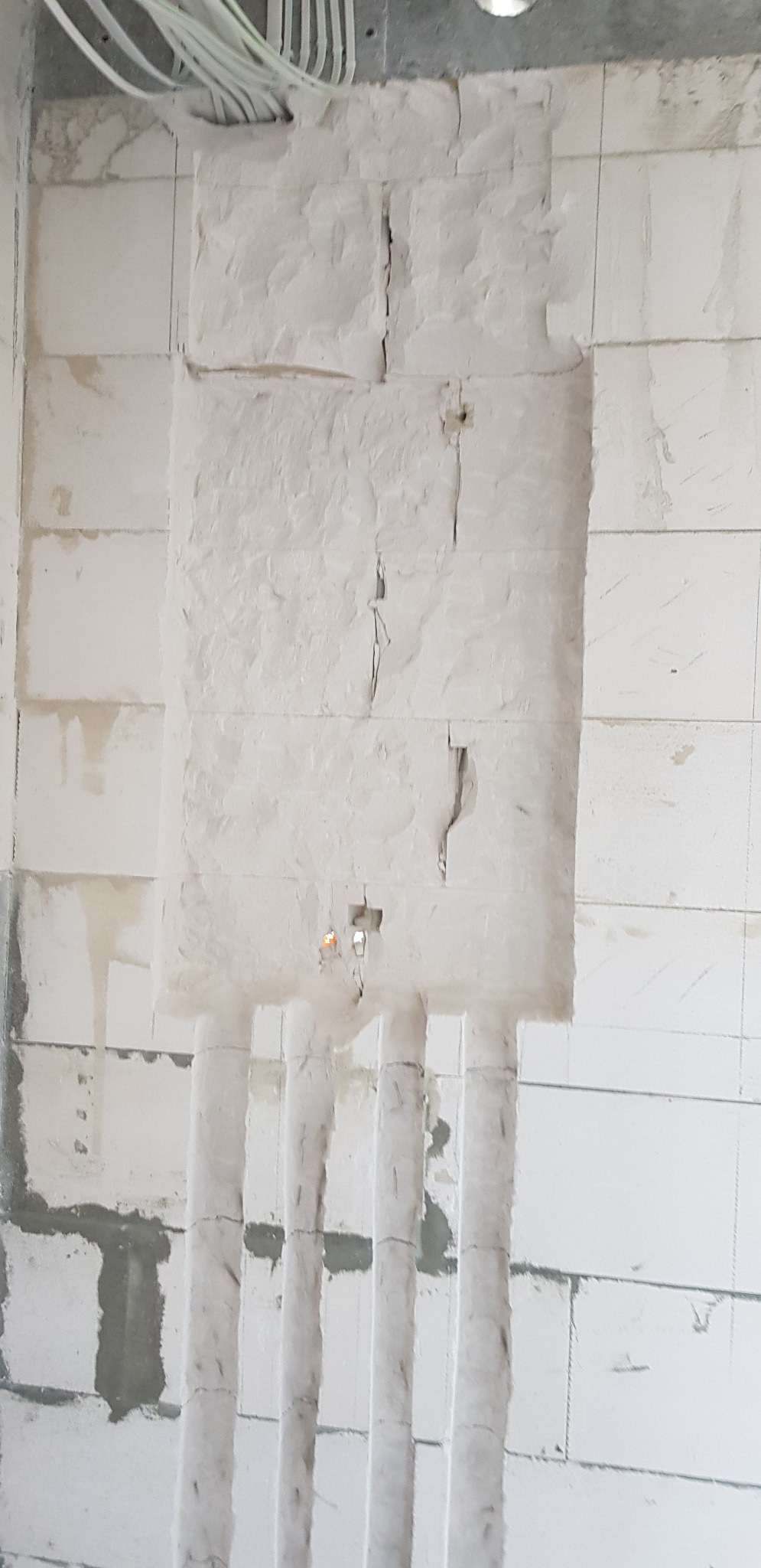 Ściana z betonu komórkowego z wyfrezowanymi bruzdami pionowymi, prawdopodobnie pod instalację elektryczną, widoczne przewody w górnej części ściany.