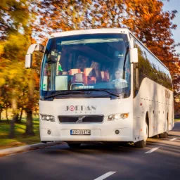 Biały autokar Jordan Group z kierowcą na drodze otoczonej jesiennymi drzewami, widok z przodu, tablica rejestracyjna KR-304TH.