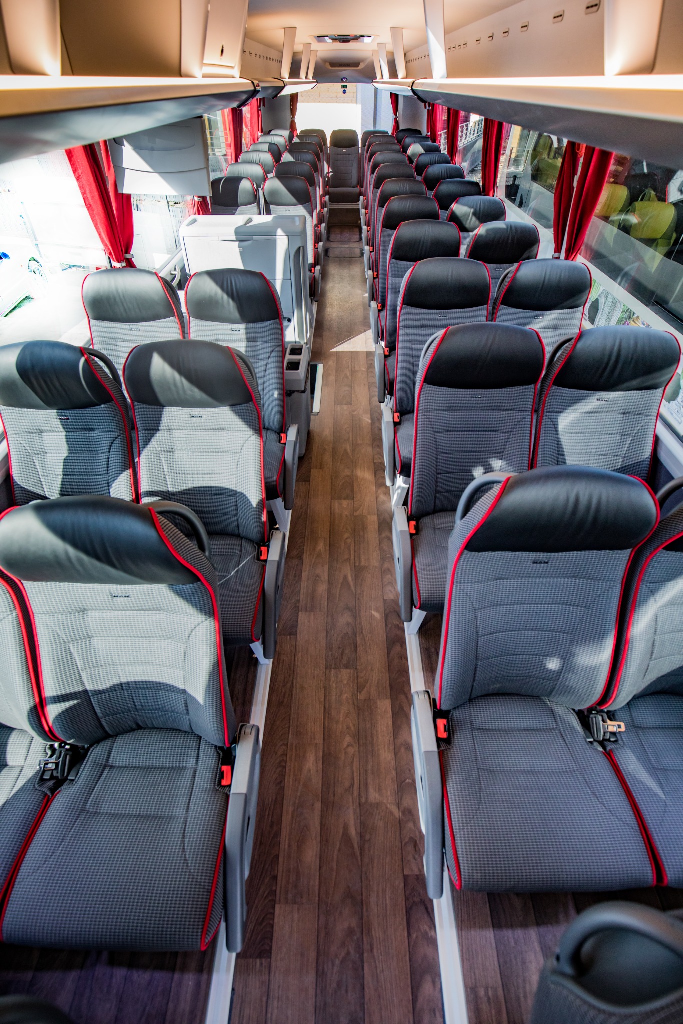 Wnętrze autobusu dalekobieżnego z rzędami szarych foteli z czarnymi zagłówkami i czerwonymi akcentami, widok z przodu na puste przejście.