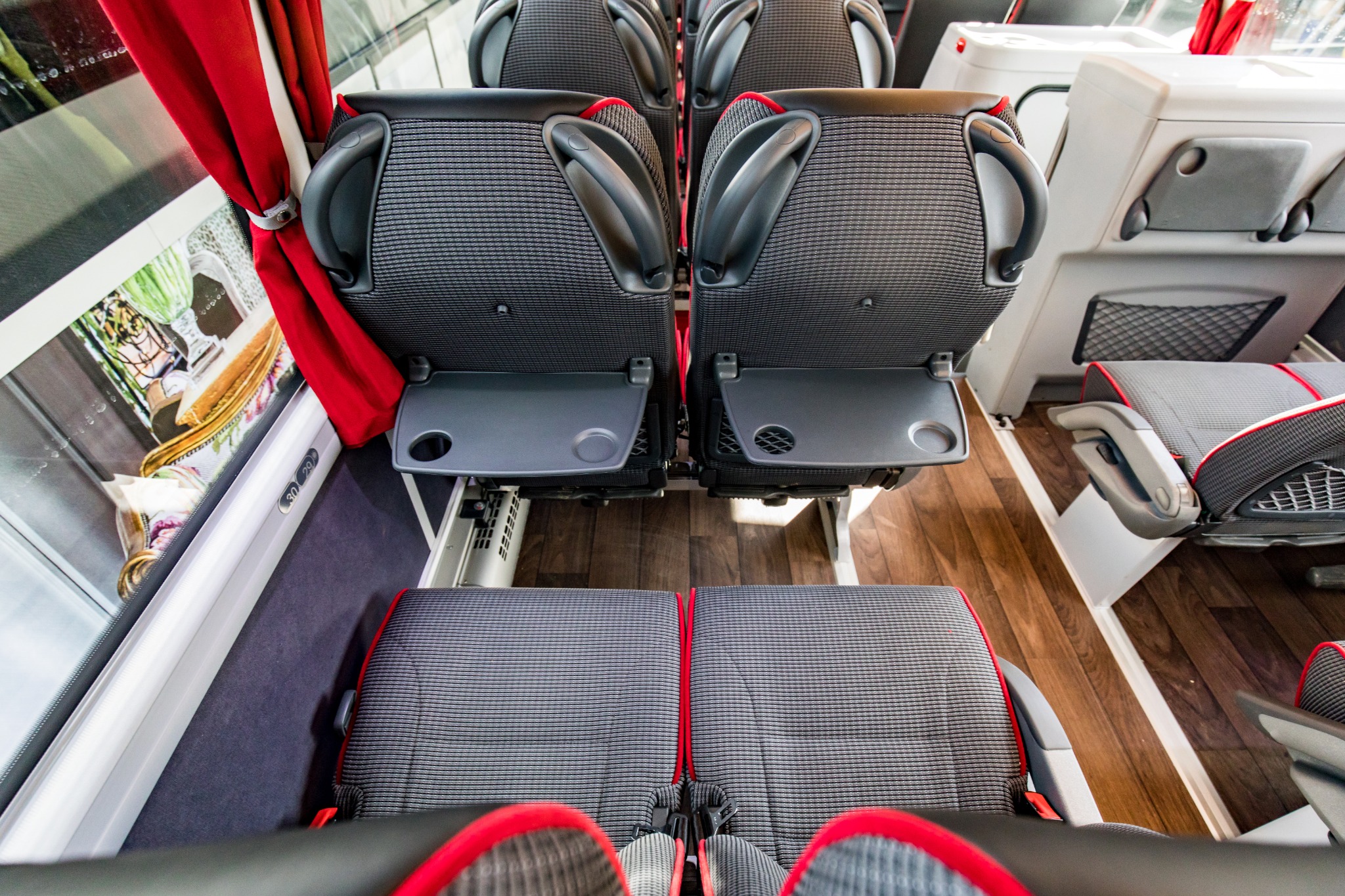 Wnętrze autobusu turystycznego: rzędy foteli z rozkładanymi stolikami, czerwone zasłonki przy oknach, widok z góry.