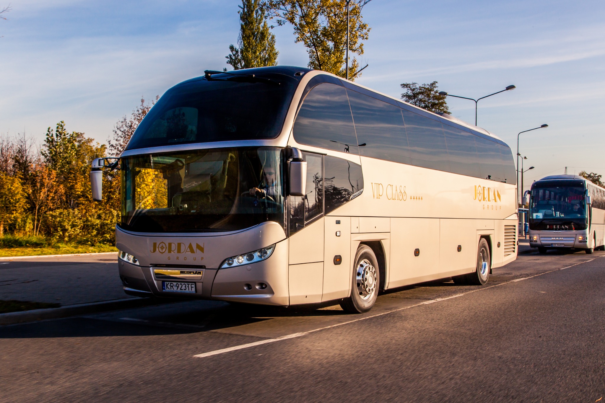 Beżowy autokar VIP Class firmy Jordan Group na drodze w słoneczny dzień, widoczny numer rejestracyjny KR 923TF.