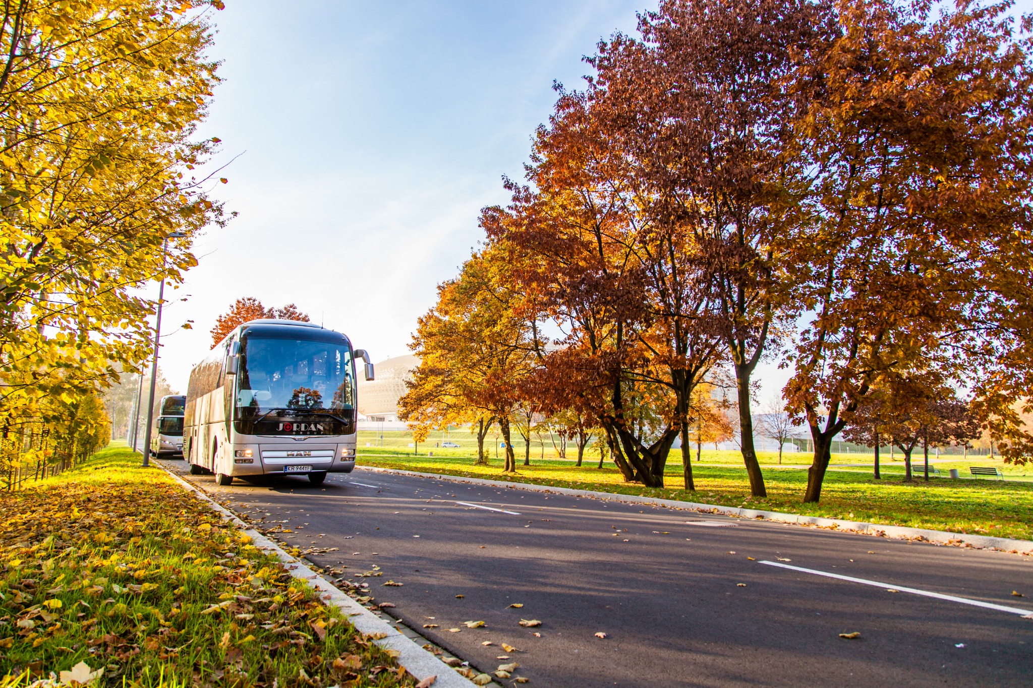 Dwa autobusy turystyczne na drodze w jesiennej scenerii, z widocznym logo 'Jordan Group' na pierwszym pojeździe.