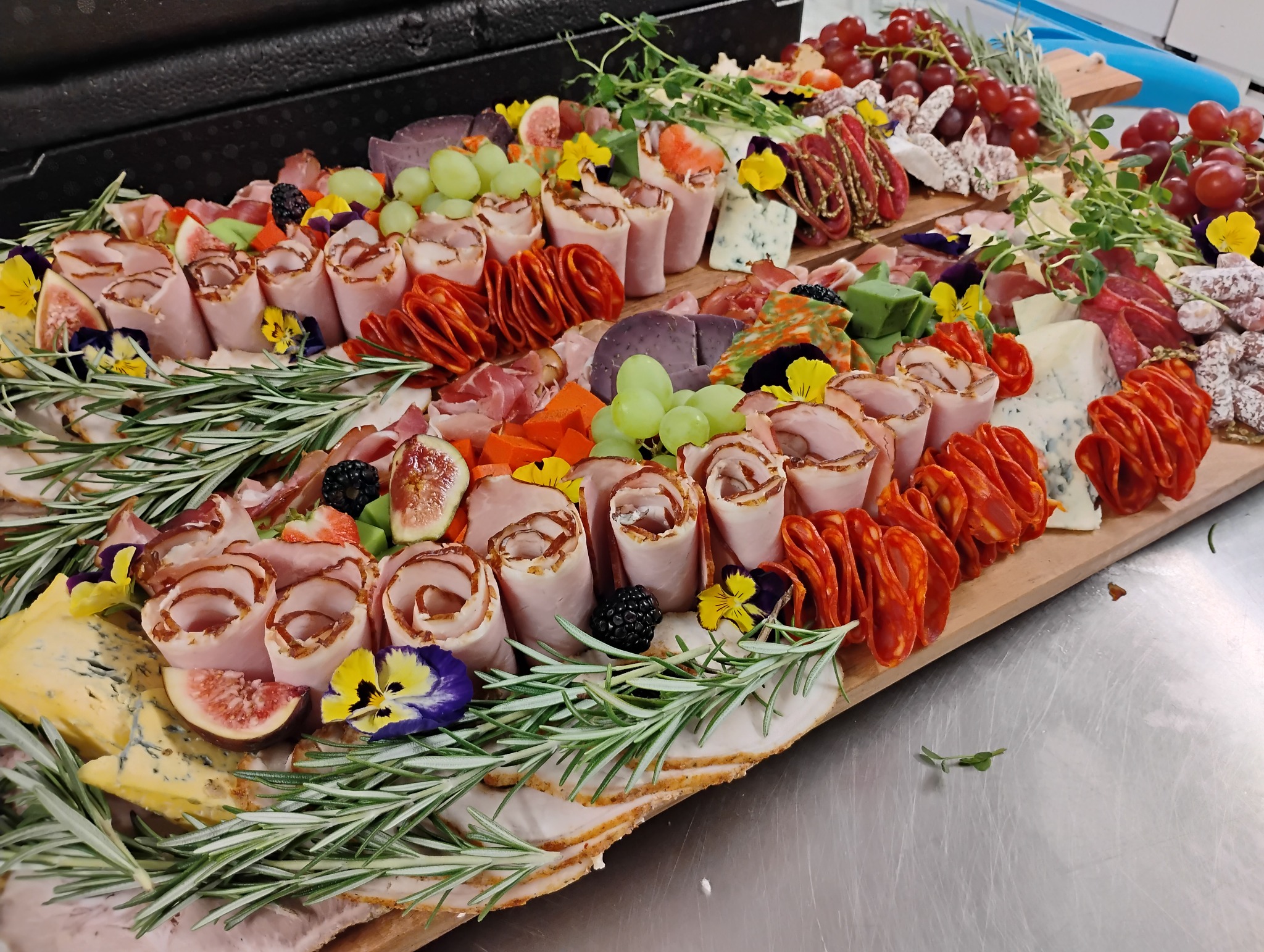 Deska serów i wędlin z dekoracjami z owoców, fig i jadalnych kwiatów, ułożona na drewnianej desce, widok z góry.