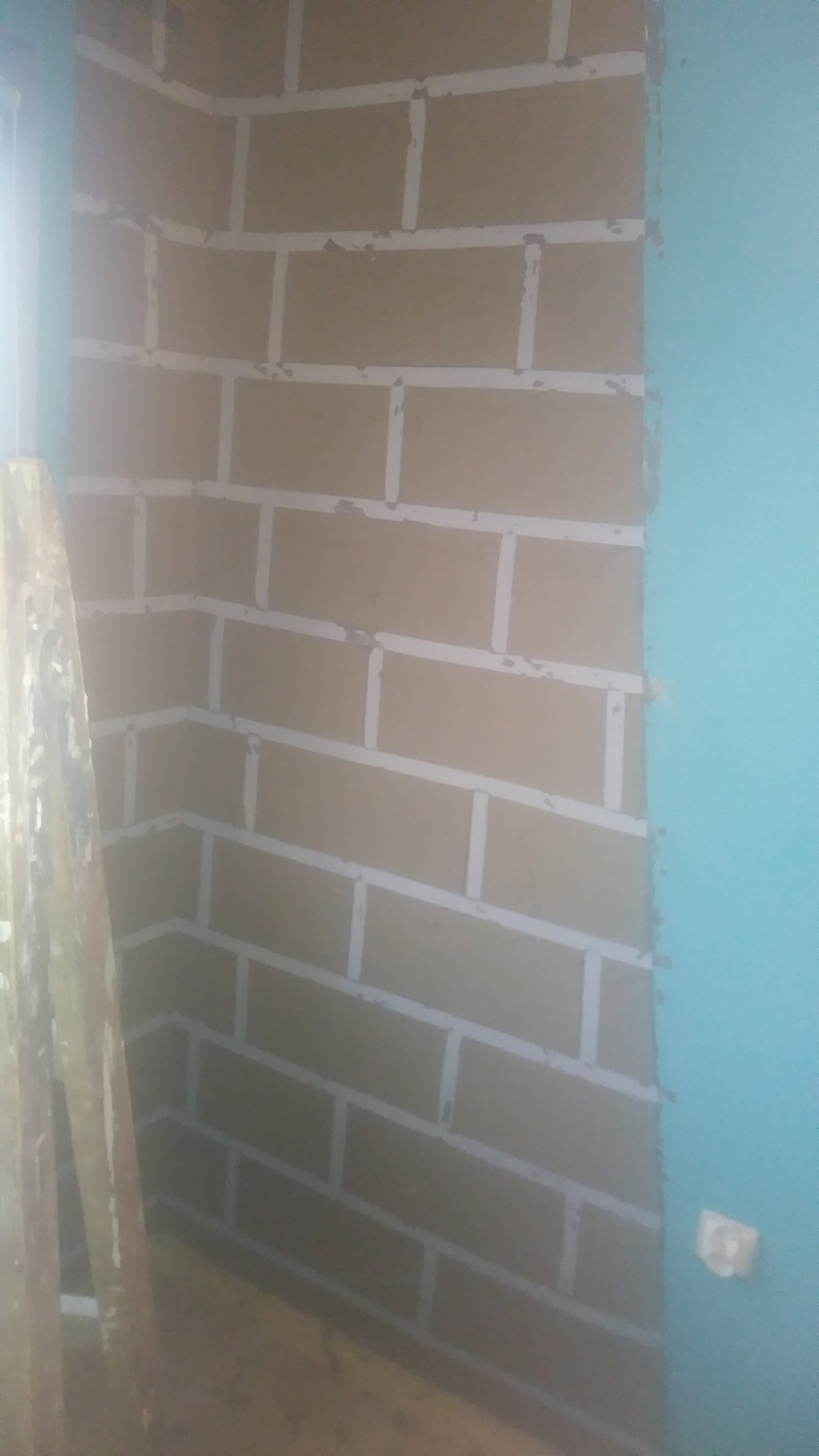 Ściana z płyt kartonowo-gipsowych, przygotowana do szpachlowania łączeń, widoczne ślady szpachli, narożnik pomieszczenia, fragment drabiny po lewej stronie.