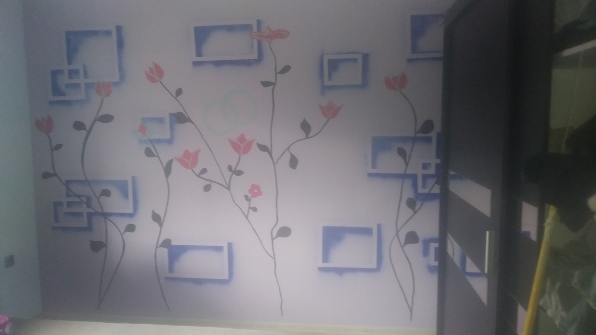 Ściana pomalowana w białe tło z motywem kwiatów i geometrycznych kształtów w odcieniach różu i błękitu, widoczne ślady po wałku.