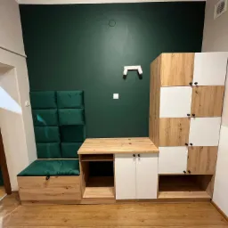Zabudowa wnęki z szafkami z frontami drewnopodobnymi i białymi, siedziskiem z zielonym obiciem i panelem ściennym z zielonych kwadratów.