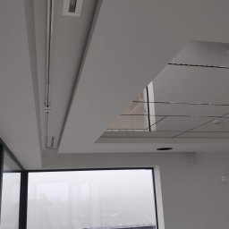 Łukasz Czarnik Mal-Mont Gips - Nowoczesne wnętrze z oknem panoramicznym, widok na zewnątrz w mglisty dzień, sufit z oświetleniem szynowym i podwieszanymi elementami.