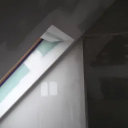 Poddasze w trakcie wykańczania: okno dachowe obudowane płytami, widoczne szpachlowanie i łączenia płyt. Ściany przygotowane do malowania, widoczne próbniki koloru.