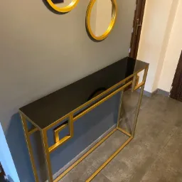 Konsola z czarnym blatem i złotą metalową konstrukcją, wykonana w Bielsko-Białej, z dekoracyjnymi okrągłymi lustrami w tle.