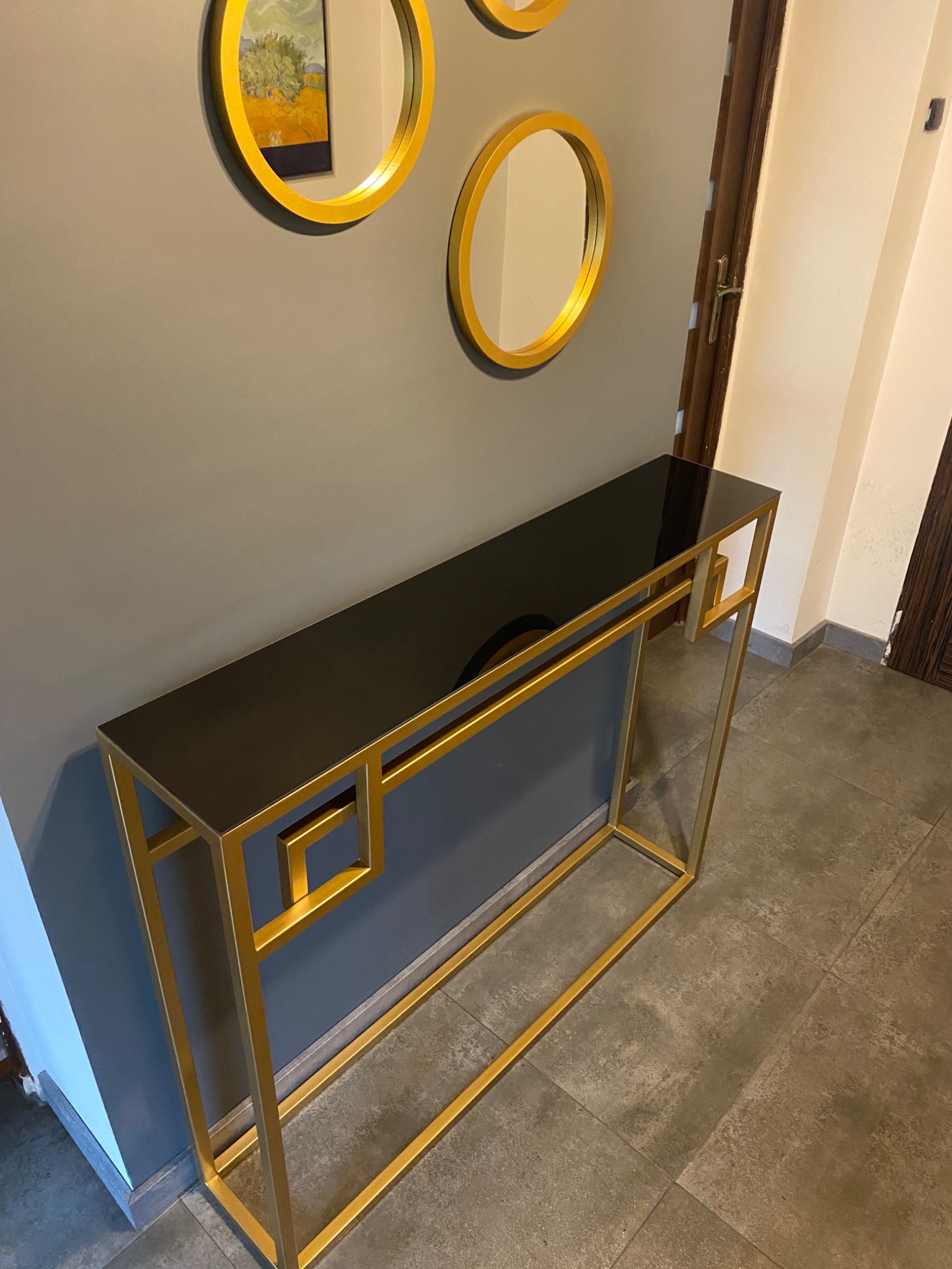 Konsola z czarnym blatem i złotą metalową konstrukcją, wykonana w Bielsko-Białej, z dekoracyjnymi okrągłymi lustrami w tle.