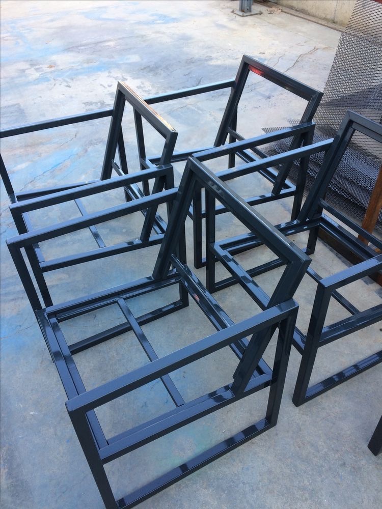 Metalowe ramy krzeseł w trakcie produkcji, spawane z profili o kwadratowym przekroju, ustawione na betonowej posadzce w warsztacie.