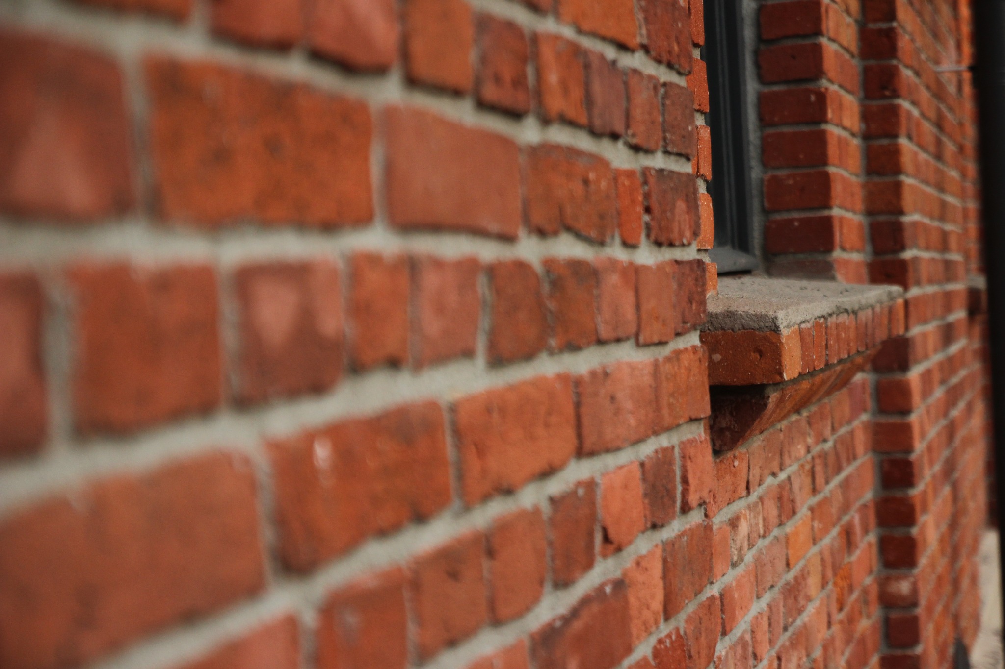 Fragment muru z czerwonej cegły z oknem, perspektywa z dołu, widoczne spoiny między cegłami.