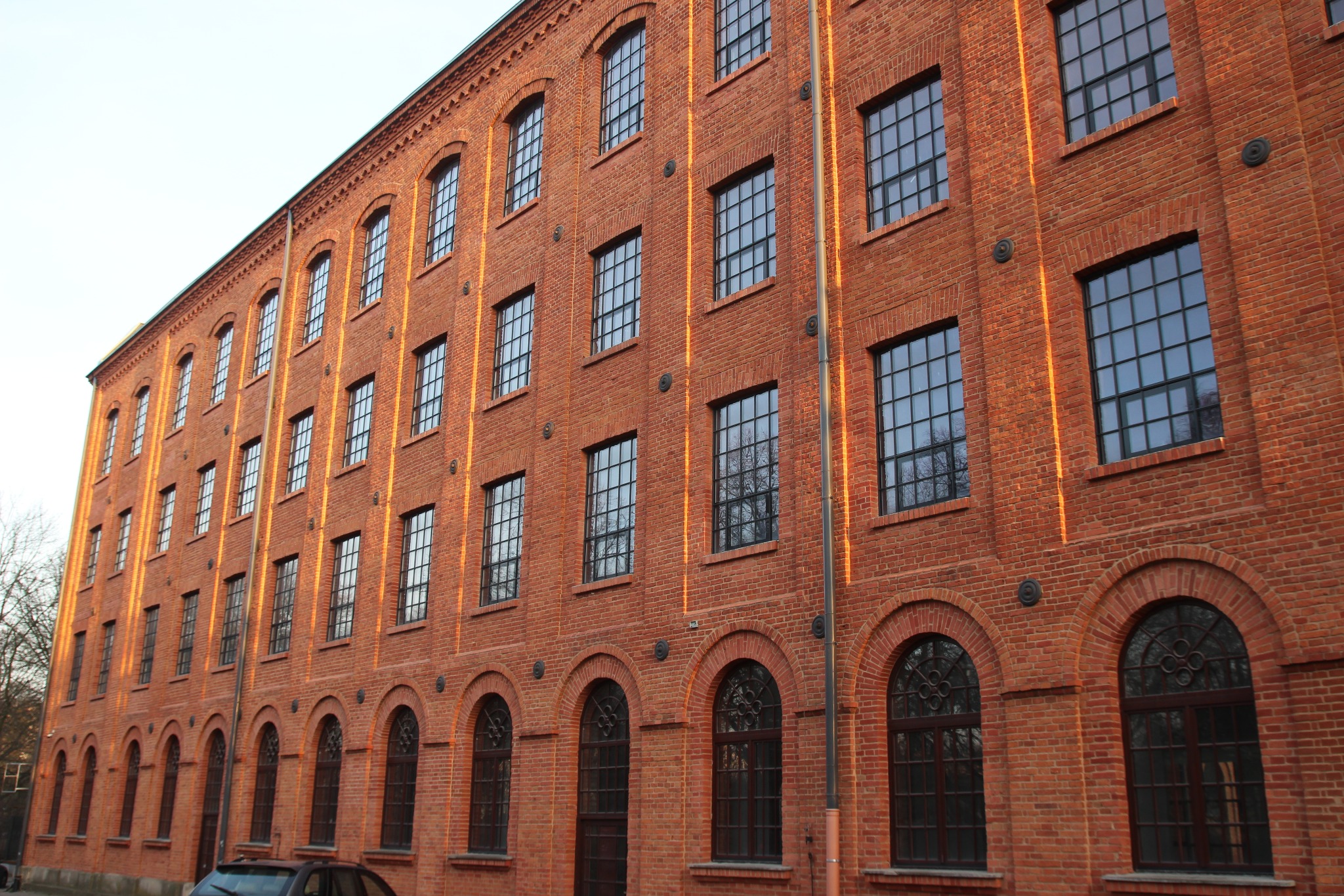 Ceglany budynek biurowy z wieloma oknami w czarnych ramach, częściowo oświetlony popołudniowym słońcem.