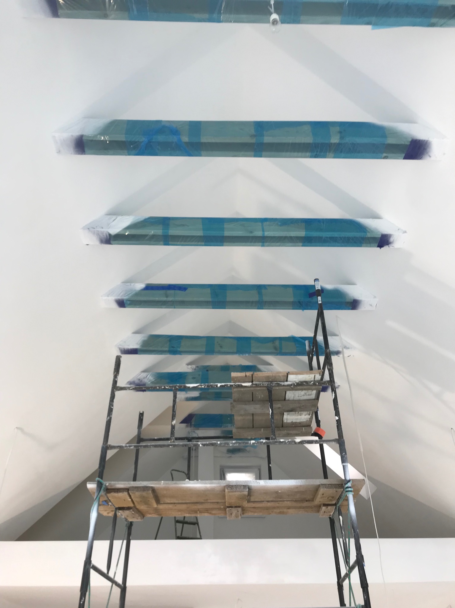 Przygotowanie do malowania sufitu w Niepołomicach: listwy przypodłogowe zabezpieczone folią i taśmą malarską, widoczny fragment rusztowania malarskiego.